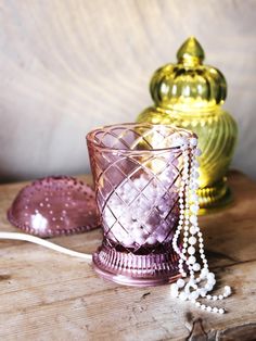 a pink glass candle holder sitting on top of a wooden table next to other decorative items