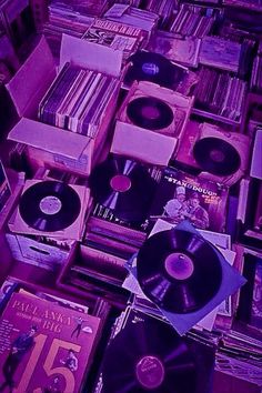 an assortment of records and cds are stacked on top of each other in purple hues