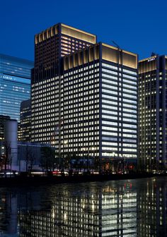 two tall buildings next to each other in front of a body of water at night