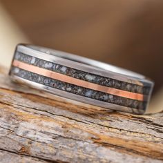 a wedding band with black and copper inlays sits on a piece of wood