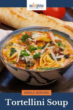 a bowl of tortellini soup on a plate with bread and tomatoes in the background