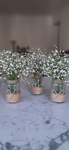 three mason jars with baby's breath flowers tied in twine on a table