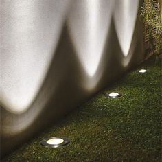 some lights that are in the grass near a wall and fence with plants growing on it