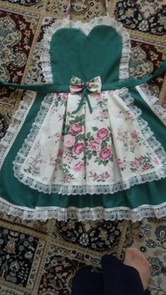 a green and white dress with pink roses on the skirt is sitting on a rug