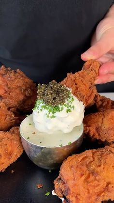 a person dipping something into a small bowl filled with sauce on top of fried chicken