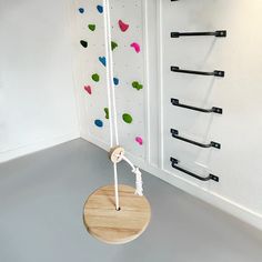 a wooden swing hanging from the side of a white wall next to a climbing wall