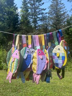 several colorfully painted birds are hanging on a clothes line in the grass with trees in the background