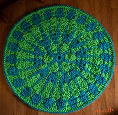 a green and blue crocheted round rug sitting on top of a wooden floor