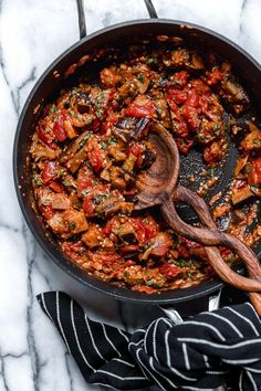 a skillet filled with meat and vegetables on top of a marble counter next to a wooden spoon