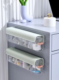 two clear plastic drawers on top of a white desk next to a vase with flowers