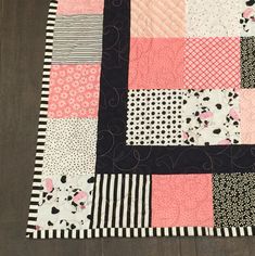 a patchwork quilt is laying on top of a wooden floor with black and white stripes