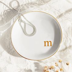 a white and gold plate with the letter m on it, next to dried flowers