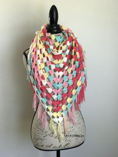 a mannequin wearing a multicolored crocheted shawl with fringes