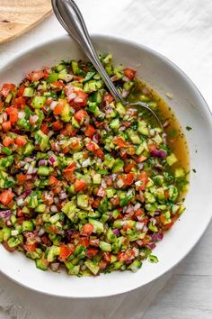 a white bowl filled with cucumber and red onion salad next to a wooden spoon