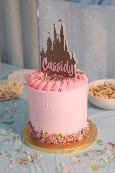 a pink cake sitting on top of a table covered in sprinkles