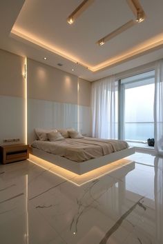 a large white bed sitting in the middle of a room next to a tall window