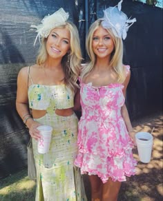 two beautiful women standing next to each other in dresses and holding coffee cups on the grass