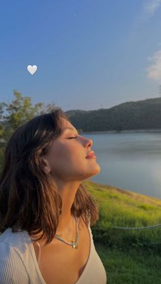 a woman looking up at the sky with a heart shaped object above her head in front of a body of water