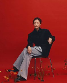 a woman sitting on a chair in front of a red wall with flowers around her