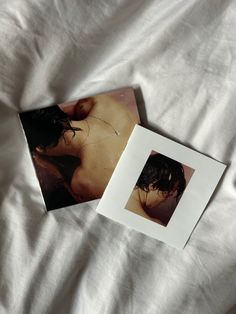 two photographs are laying on top of a white bed sheet, one is naked and the other is unbuttoned