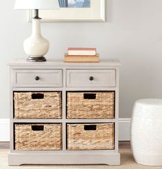 a white dresser with wicker baskets on top and a lamp next to it in a room