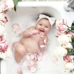 a baby is taking a bath in a sink with flowers around it and smiling at the camera