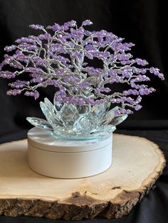 a glass vase filled with purple flowers sitting on top of a wooden slice next to a black background