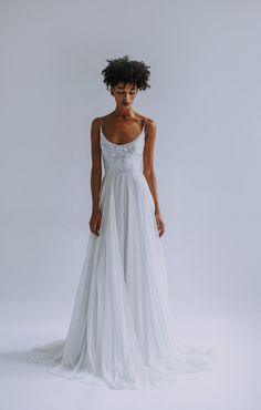 a woman in a white wedding dress standing with her back turned to the camera and looking off into the distance