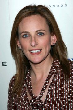 a woman with long hair wearing a brown and white dress shirt smiling at the camera