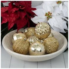 gold christmas ornaments in a white bowl on a table next to poinsettis