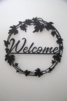 a metal sign that says welcome hanging from the side of a wall with leaves on it