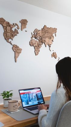 a woman sitting in front of a laptop computer on top of a desk next to a wooden world map