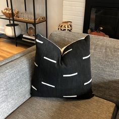 a black and white pillow sitting on top of a gray couch next to a fire place