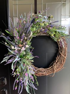 a wreath with purple flowers and greenery hangs on the front door to welcome guests