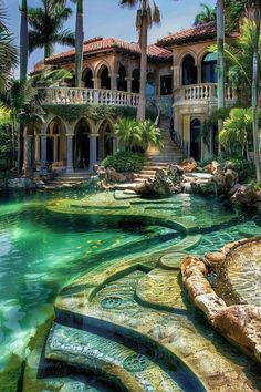 a large house that is surrounded by palm trees and green water in front of it