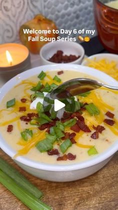 a bowl of soup with bacon, cheese and celery in it next to a candle