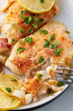 two pieces of fish on a plate with lemon wedges and parsley garnish