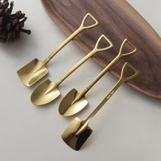 three gold utensils sitting on top of a wooden plate next to pine cones