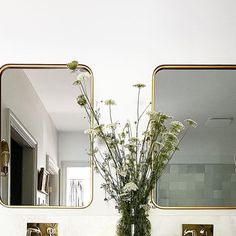 a vase with flowers sitting on top of a bathroom sink next to two mirrors above it