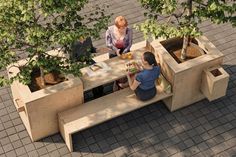 two people sitting at a table with plants in the middle and one person standing next to them