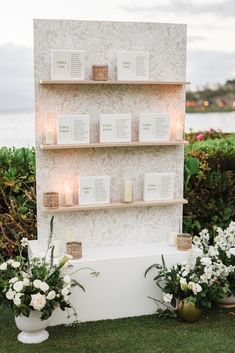 candles and flowers are on display in front of a white wall with floral arrangements around it