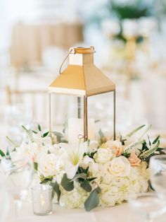 a table topped with white flowers and a small lantern on top of it's centerpiece