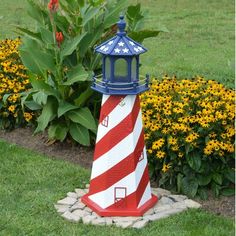 a red, white and blue lighthouse is in the grass next to some yellow flowers