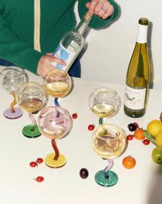 a woman pouring wine into glasses with fruit on the table next to it and bottles