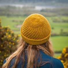 a woman with long hair wearing a yellow knitted hat looking out over the countryside