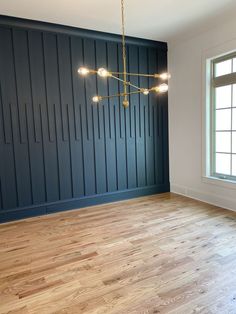 an empty room with wood flooring and blue painted paneling on the walls, along with a chandelier