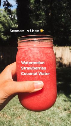 a hand holding a jar of watermelon strawberries coconut water