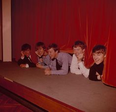 five young men sitting on the floor in front of a red curtain