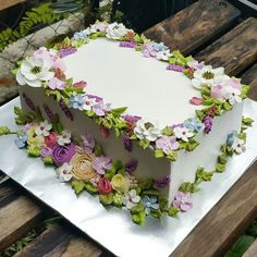 a white cake with flowers on it sitting on top of a wooden table next to a bench