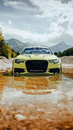 a yellow sports car parked in the middle of a muddy road with mountains in the background